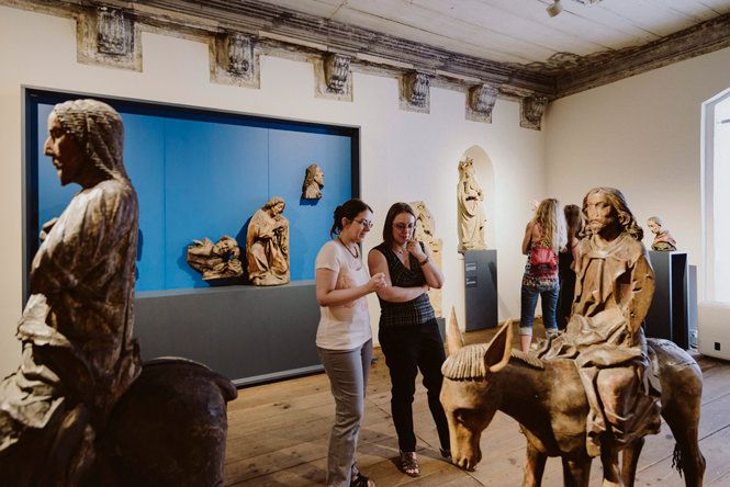 Ausstellungsraum mit historischen Figuren (eine Person reitet auf einem Pferd, eine reitet auf einem Esel). In der Mitte sthen 2 Personen und betrachten die Statuen.